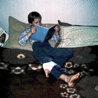Boy reading book on couch with legs stretched out.