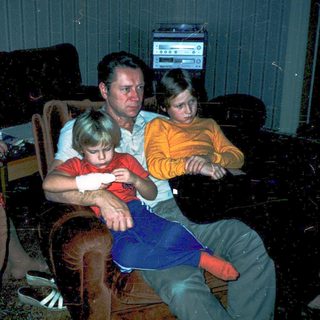 Family gathered indoors watching television in dim lighting.