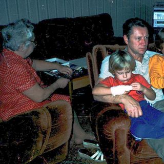 Family gathered indoors watching television in dim lighting.