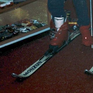Two children indoors practicing skiing with poles.