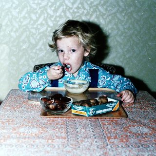 Child eating dessert with spoon indoors.