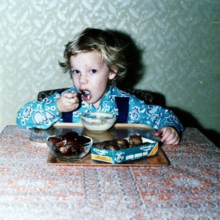 Child eating dessert with spoon indoors.
