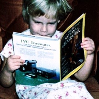 Child reading book on armchair in living room.