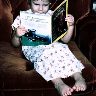 Child reading book on armchair in living room.