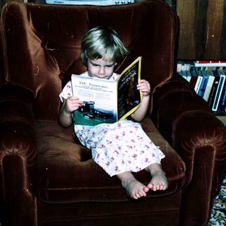 Child reading book on armchair in living room.