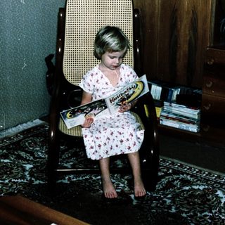 Young girl reading book in vintage chair.