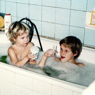 Two children playing in a bathtub with bubbles.