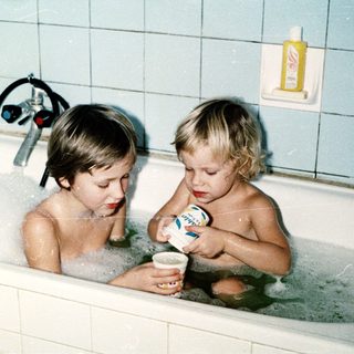 Two children playing in a bathtub with bubbles.