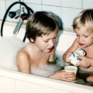 Two children playing in a bathtub with bubbles.