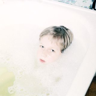 Child relaxing in a bathtub filled with bubbles.