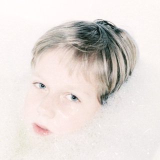 Child relaxing in a bathtub filled with bubbles.