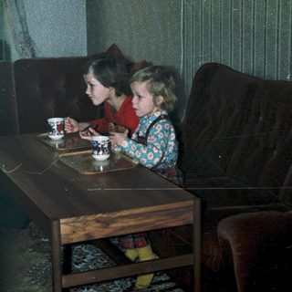 Two children drinking tea indoors at a small table.