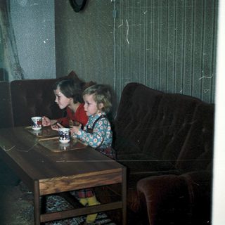 Two children drinking tea indoors at a small table.