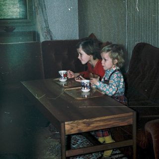 Two children drinking tea indoors at a small table.