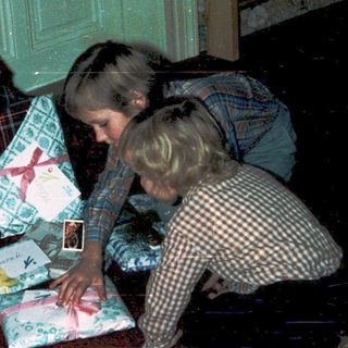 Two children opening wrapped holiday gifts indoors.