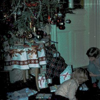 Children opening Christmas presents under decorated tree.