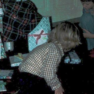 Children opening Christmas presents under decorated tree.