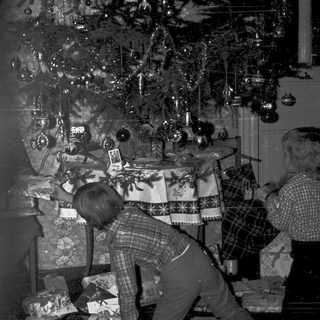 Family decorating Christmas tree with wrapped gifts.