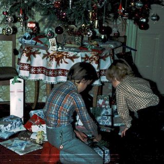 Two children decorating Christmas gifts under a decorated tree.