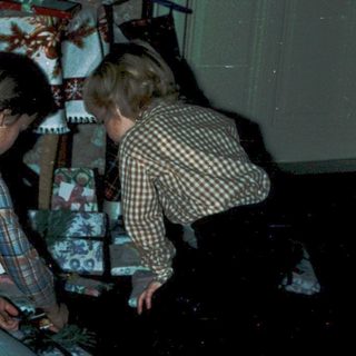 Two children decorating Christmas gifts under a decorated tree.
