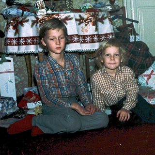 Two children sitting under decorated Christmas tree.