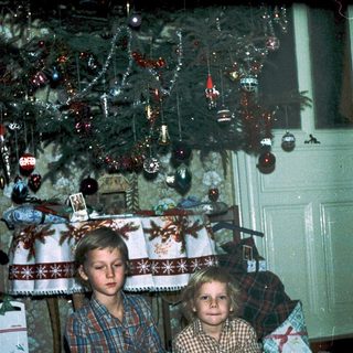 Two children sitting under decorated Christmas tree.
