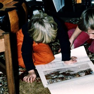 Two children examining a large map together indoors.