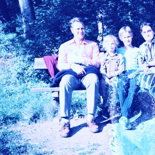 Family posing together outdoors on park bench.