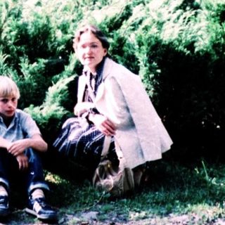 Four people sitting outdoors among green shrubs.