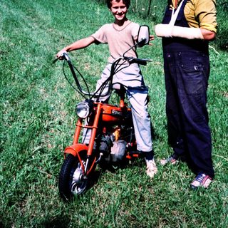 Young boy with adult on moped in rural field.