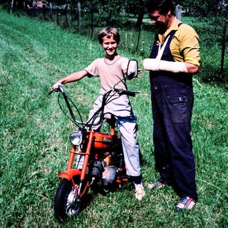Young boy with adult on moped in rural field.