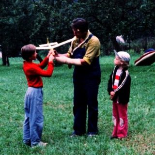 Family playing frisbee in rural orchard field.