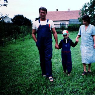 Family walking hand-in-hand in rural grassy field.