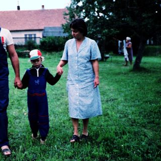 Family walking hand-in-hand in rural grassy field.