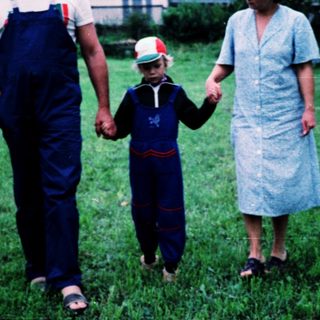 Family walking hand-in-hand in rural grassy field.