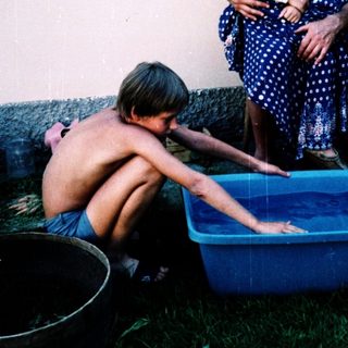 Children playing with water in a plastic tub outdoors.