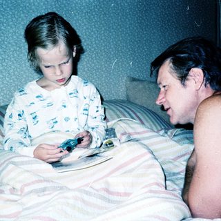 A man and young girl playing video game together in bed.