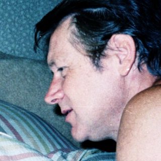 A man and young girl playing video game together in bed.