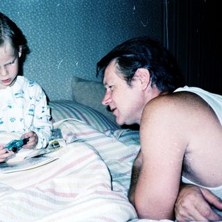A man and young girl playing video game together in bed.