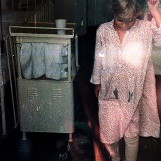 Woman in hospital gown drying hair in dimly lit room.