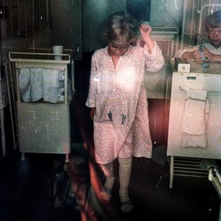 Woman in hospital gown drying hair in dimly lit room.