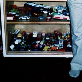 Boy in overalls poses with toy vehicles.