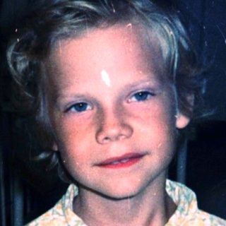 Young boy in pajamas standing indoors near metal railing.