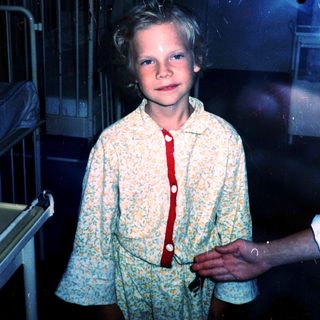 Young boy in pajamas standing indoors near metal railing.