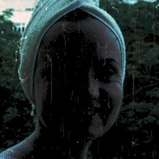 Wet person standing outdoors in rain, wearing headscarf.