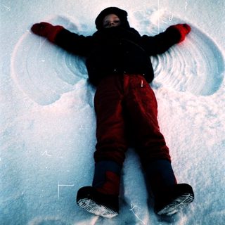 Child lying on snow with arms outstretched.