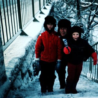 Three people dressed warmly walking on snowy stairs.