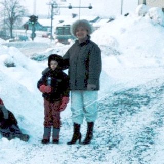 Snowy city intersection with three people near piled snow.