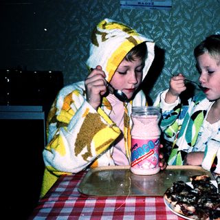 Two children in aprons eating pizza and drinking.