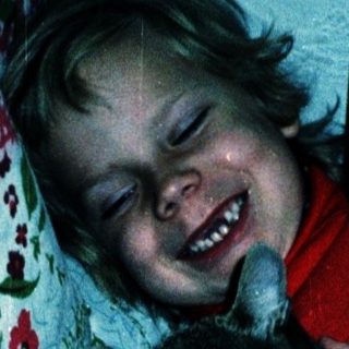 Child hugging a black cat on bed.
